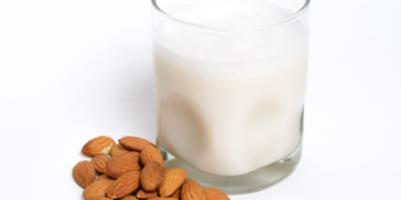 Mleko migdałowe w szklance wraz z rozsypany obok migdałami